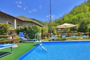 Piscina com espreguiçadeiras, cerca de madeira e um edifício com um relógio.
