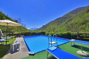 A swimming pool with a view of mountains, a wooden deck, and lounge chairs. - Casa Le Meriche (Castiglione di Garfagnana)