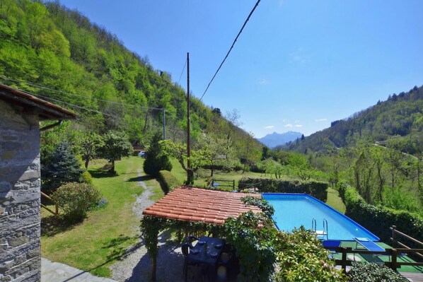 A swimming pool with a red roof, surrounded by lush greenery and hills. - Casa Le Meriche (Castiglione di Garfagnana)