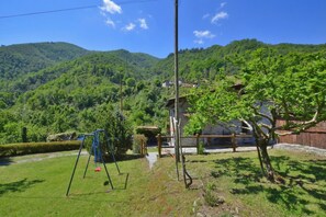 Uma casa de campo com jardim, baloiço e vista para colinas verdes.
