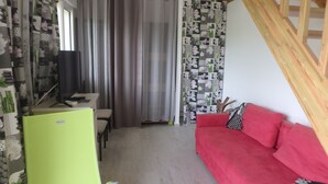 Ein Zimmer mit einem roten Sofa, einem Schreibtisch mit Computer, einem grünen Sessel und einem gemusterten Vorhang.