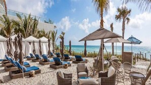 Un espace de détente aménagé au bord de la plage, avec des chaises longues et des fauteuils en osier, offrant une vue sur l’océan.