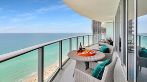 Un balcon avec une table ronde, des meubles en osier et une vue sur la plage et l’océan.