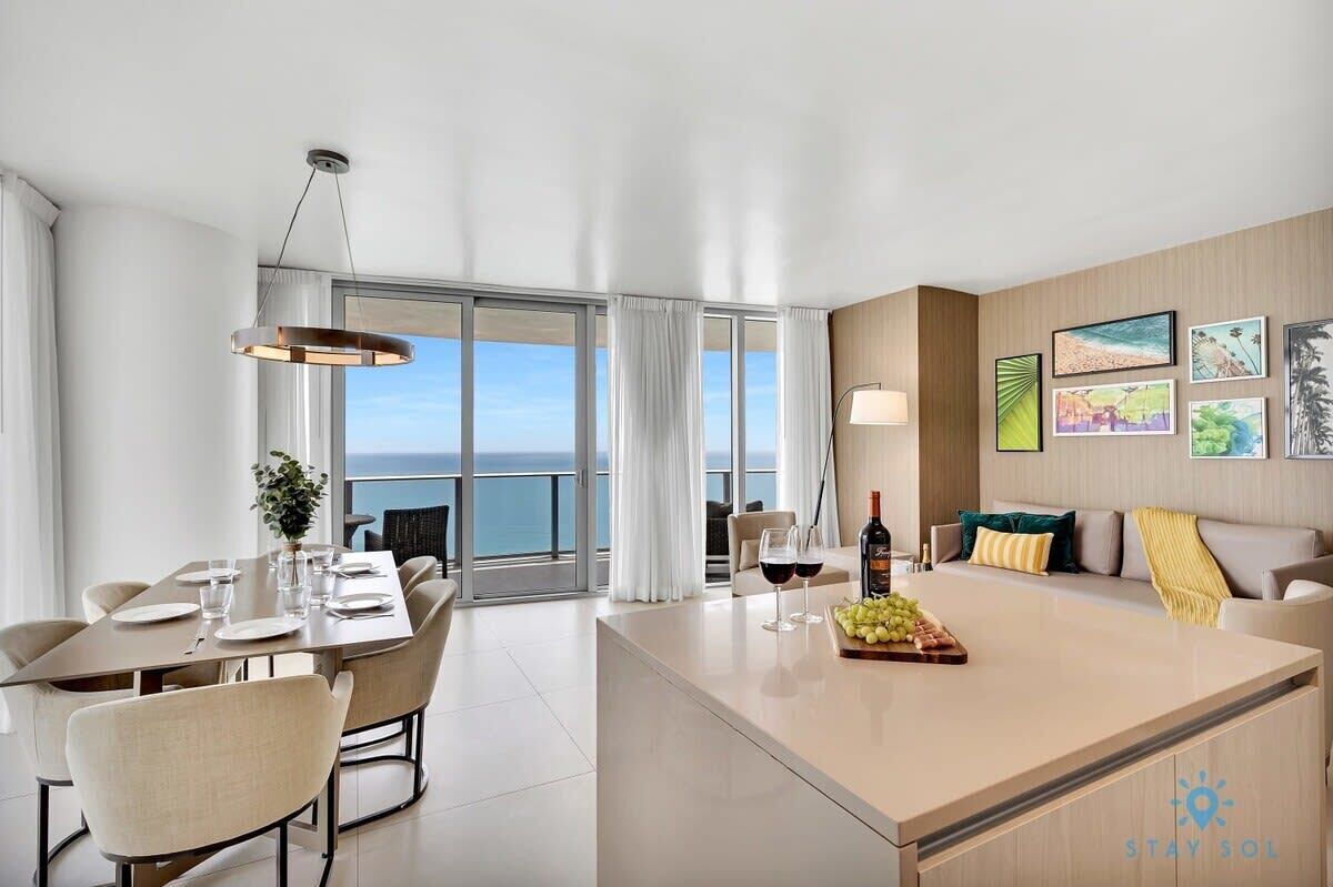 A modern hotel room with a dining area, a sofa, and a view of the sea.