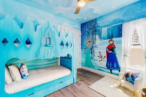 Une pièce décorée d’une fresque aux motifs bleus, avec un lit, une fenêtre avec des rideaux et une chaise blanche.