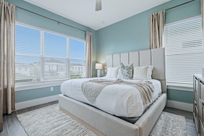 Quarto com uma cama grande, uma mesa de cabeceira, um abajur e vista para o exterior.