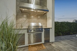 An outdoor kitchen with a stainless steel range hood, a built-in oven, and a refrigerator.