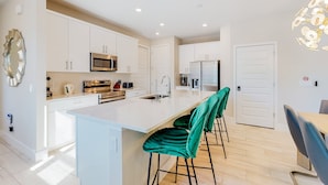 A modern kitchen with white cabinets, stainless steel appliances, a central island with bar stools, and a dining area with a table and chairs.