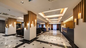 Un vestíbulo de hotel moderno con suelo de mármol, detalles de madera y un mostrador de recepción.