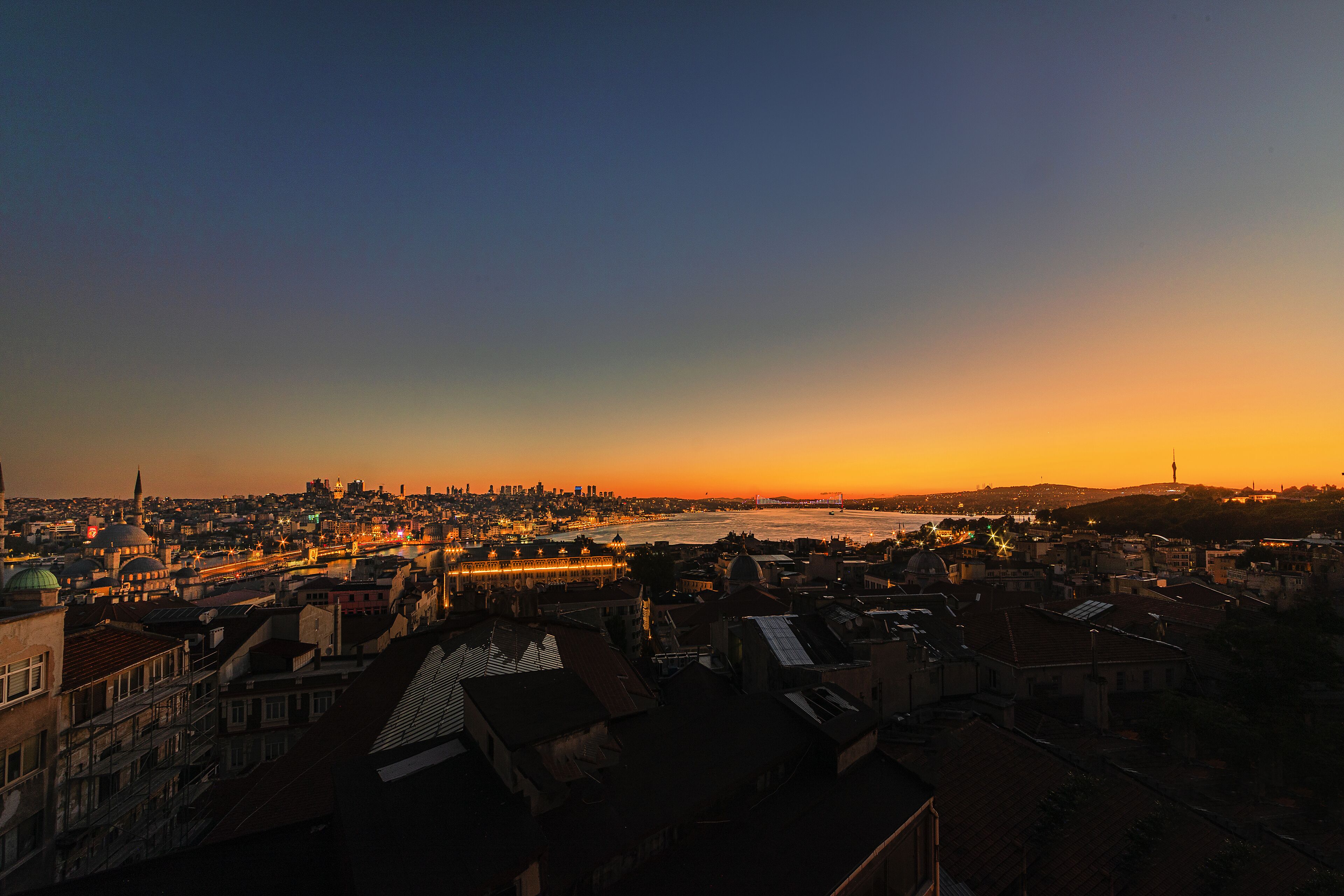 A cityscape at sunset with a river, buildings, and a bridge.