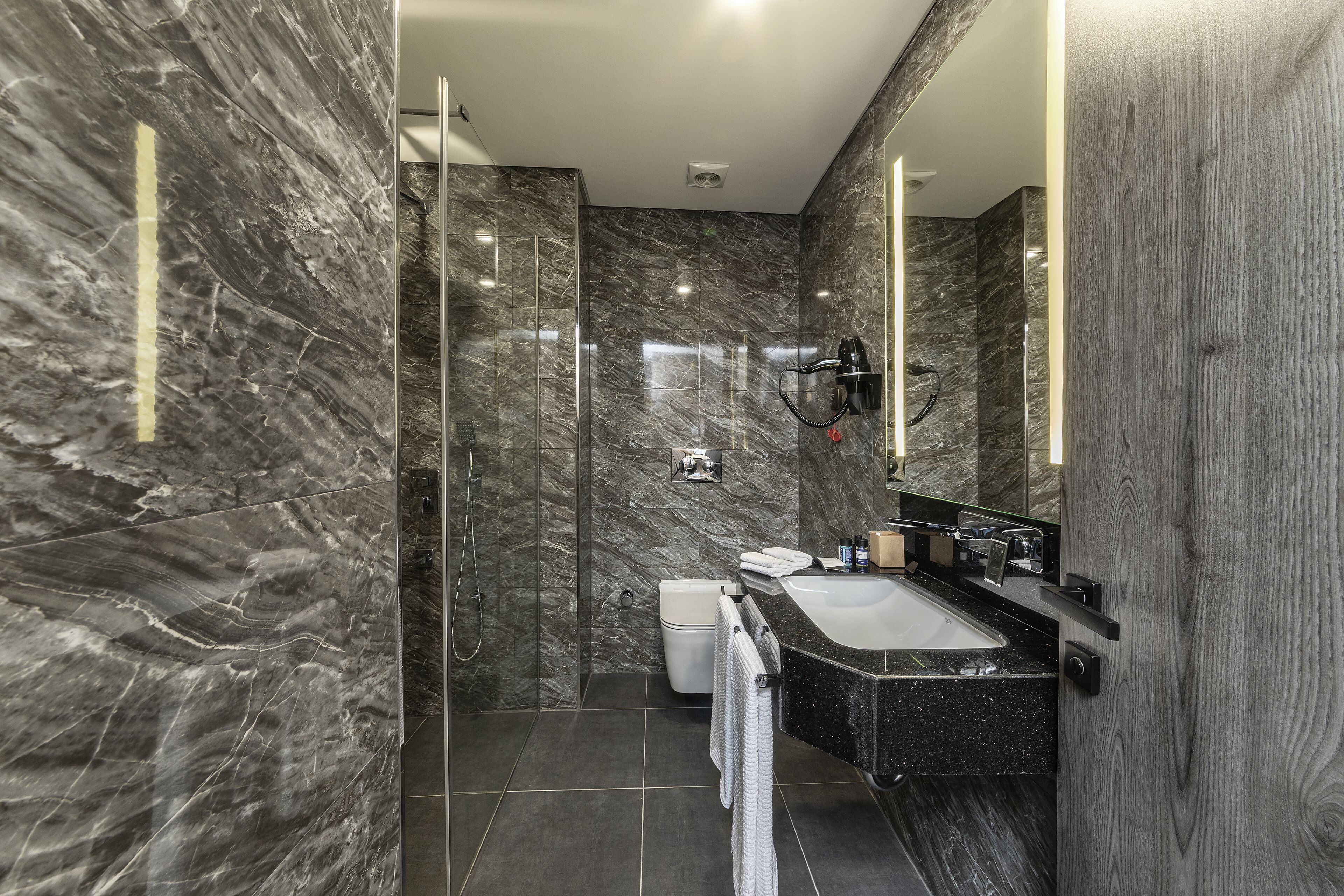 Un baño moderno con ducha de mármol, inodoro y lavabo con espejo.