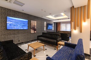 A modern lobby with a large flat-screen TV, comfortable seating, and a patterned wall.