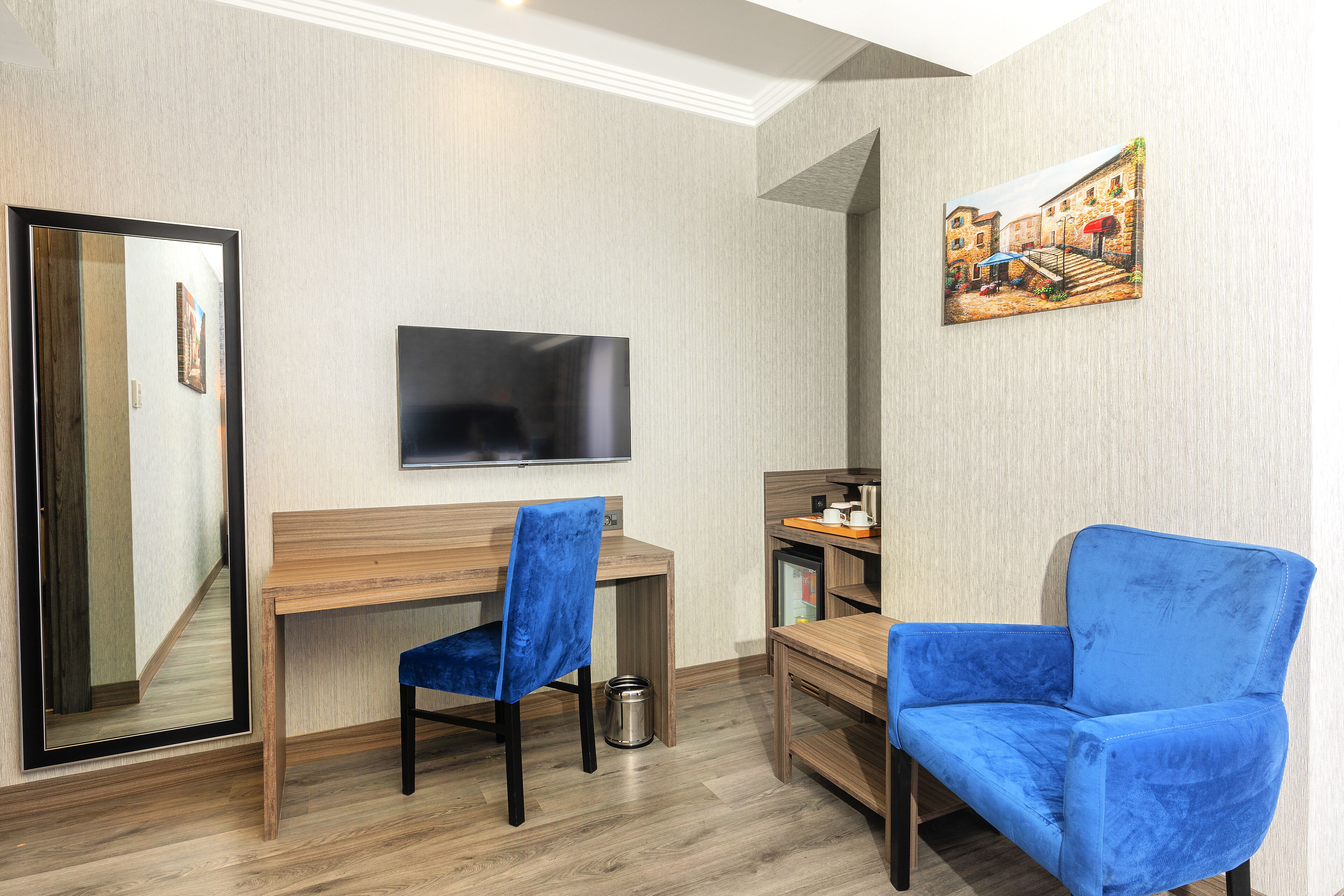 A room with a wooden desk, a blue chair, a television, and a painting on the wall.