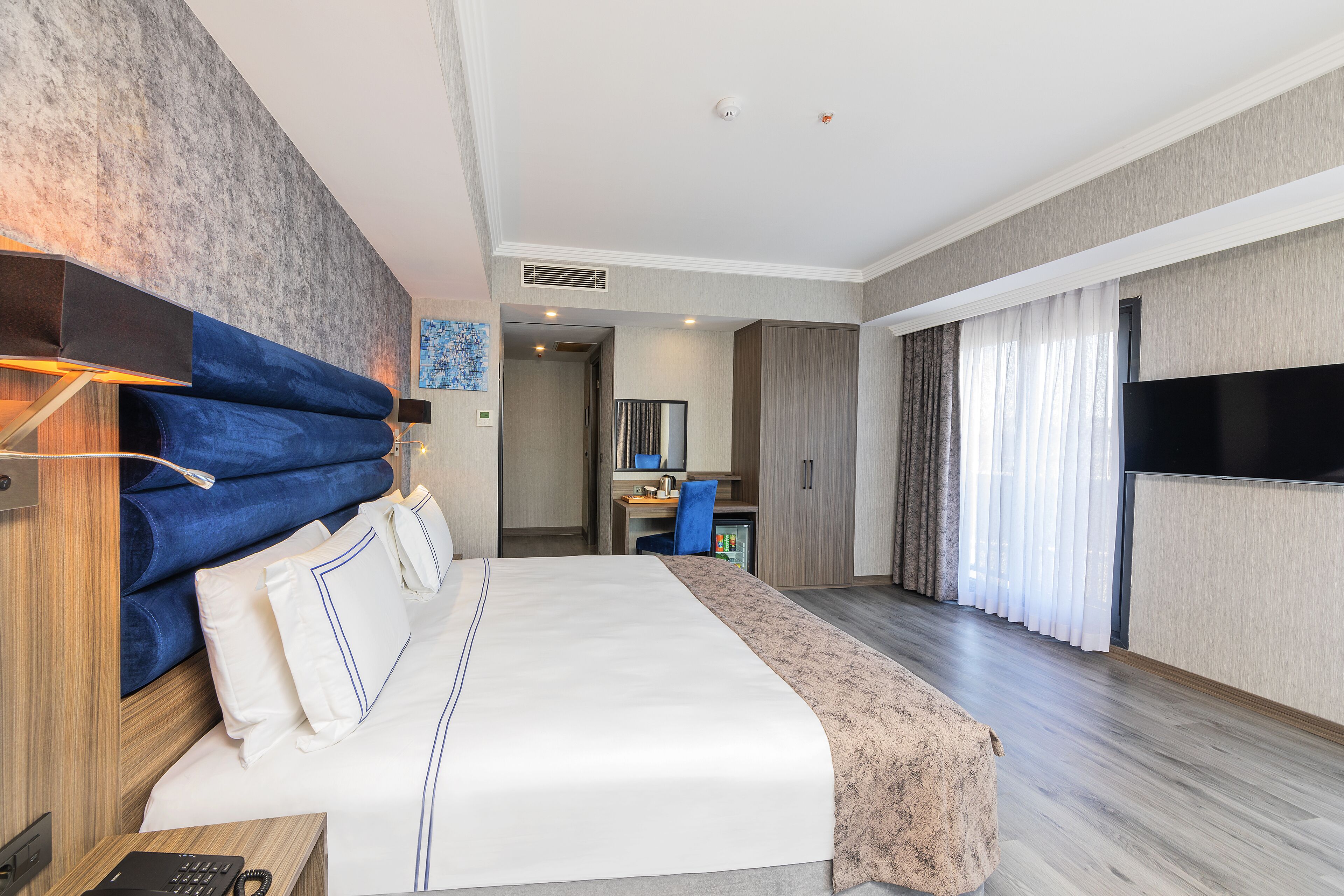Habitación de hotel con una cama grande, un escritorio, un televisor y un baño visible a través de una puerta abierta.