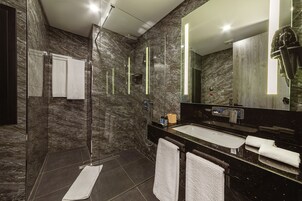 A modern bathroom with a glass shower enclosure, a large mirror, and a black countertop with a sink.
