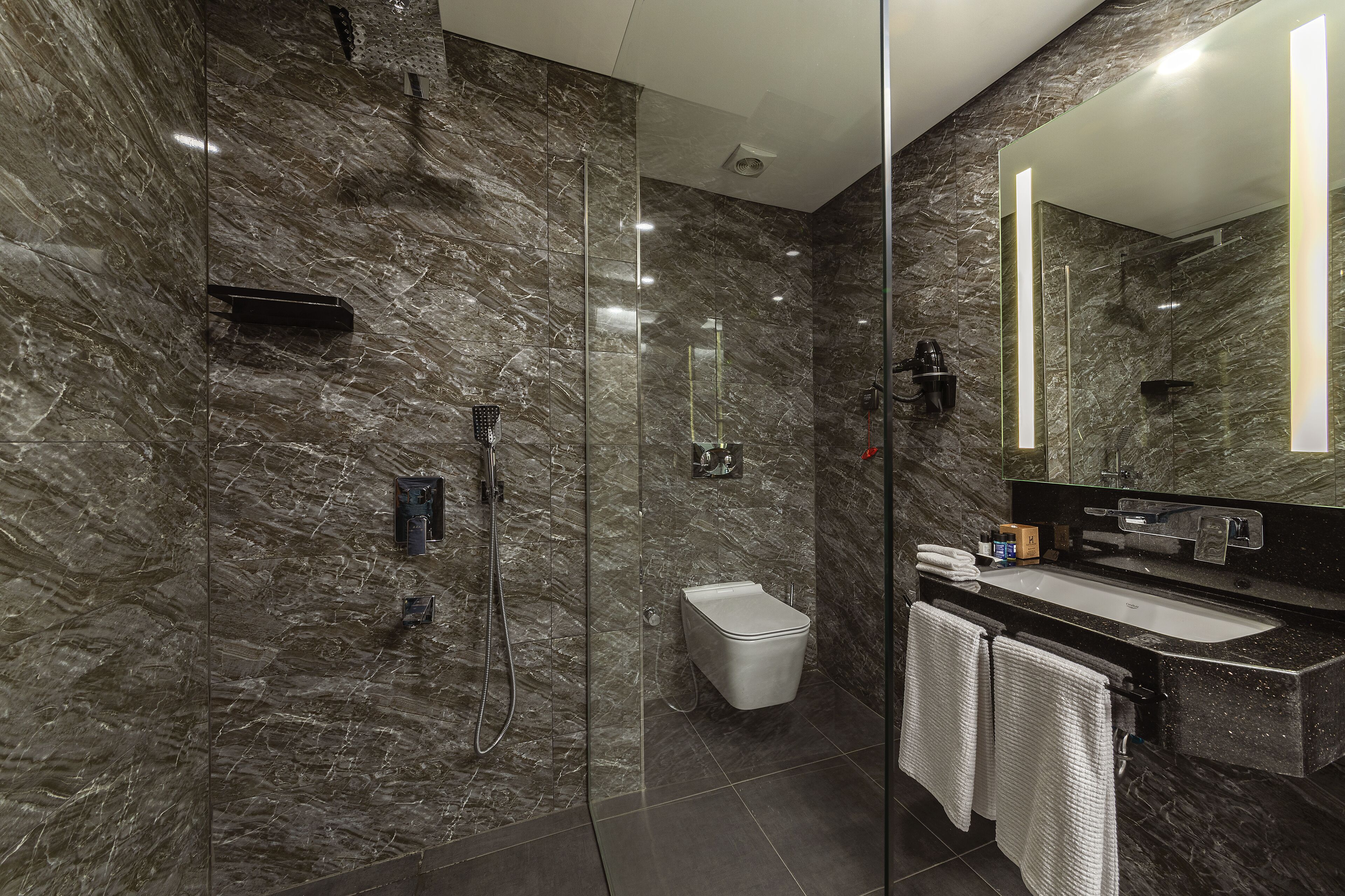 Ein modernes Badezimmer mit einer gläsernen Dusche, einer weißen Toilette und einem Waschbecken mit großem Spiegel.
