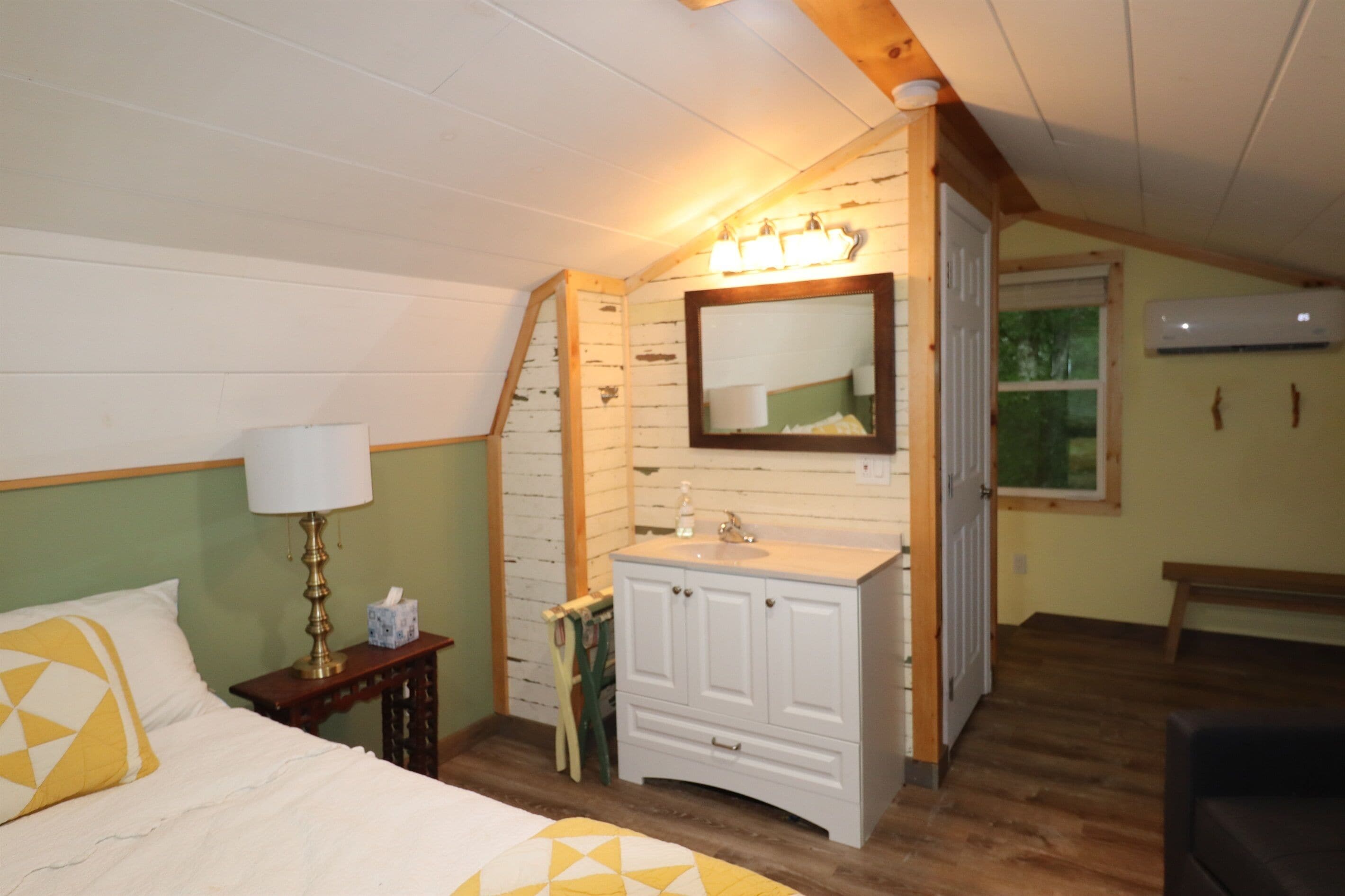 A bedroom with a bed, bedside lamp, vanity with mirror, and wooden ceiling beams.