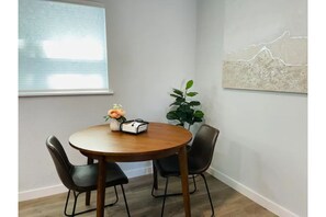 Cozy room with a round table, four chairs, and a potted plant, offering a view of the sky.