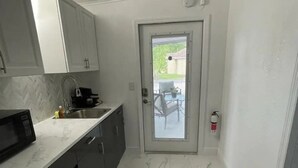 Una cucina compatta con mobili bianchi, pavimento in marmo e una porta che dà su un patio.