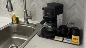 Una cucina con lavello in acciaio inossidabile, un rubinetto moderno, una macchina da caffè e una parete rivestita con piastrelle a spina di pesce.