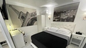 A bedroom with a bed, a nightstand, a dresser, a mirror, and a wall with a large picture.