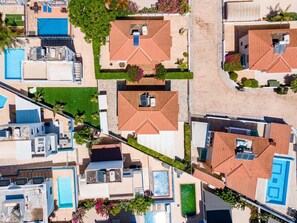 Une vue aérienne d’un quartier résidentiel composé de plusieurs maisons, chacune dotée d’une piscine, d’un patio couvert et d’un jardin.