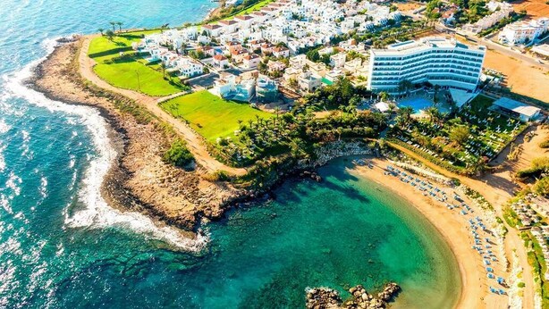 An aerial view of a coastal resort with a beachfront, a large hotel, and a golf course. - Villa Serena Springs by Ezoria Villas (Protaras)