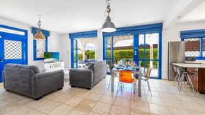 A spacious living area with a dining table set for four, a kitchen area with a refrigerator, and a seating area with two sofas. - Villa Serena Springs by Ezoria Villas (Protaras)
