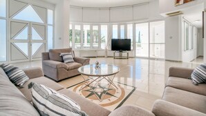 Amplia sala de estar con televisor grande, asientos cómodos y ventanas grandes que ofrecen vistas al exterior.