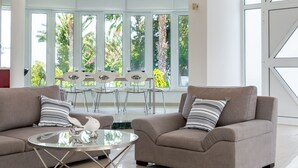 Una sala de estar moderna con un sofá color beige, una mesa de centro de vidrio y una zona de comedor con una mesa y sillas blancas.