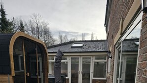 En inglasad uteplats med en träkonstruktion, en glasdörr och ett klinkergolv.