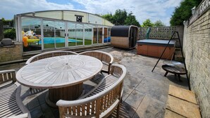 A patio with a round wooden table and chairs, a hot tub, and a covered swimming pool area. - Rentmyspahome With Swimming Pool, Hottub and Sauna (Sheffield)