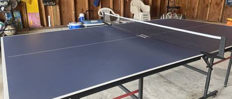 Une table de ping-pong avec un filet, entourée de divers équipements sportifs et d’un mur en bois.