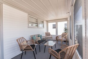 A covered porch with wicker furniture, a glass table, and a view through a screened window. - Family-Friendly Beach Home - Steps to Beach & Bay - Porch, Yard, Garage (Brigantine)