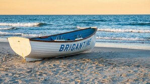 Un bote llamado "BRIGANTINE" en una playa arenosa con el océano al fondo.