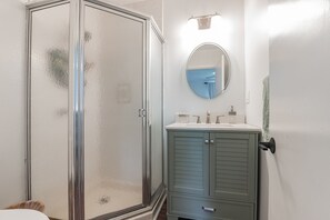 A bathroom with a glass shower enclosure, a round mirror, and a light blue vanity with a sink and countertop. - Family-Friendly Beach Home - Steps to Beach & Bay - Porch, Yard, Garage (Brigantine)