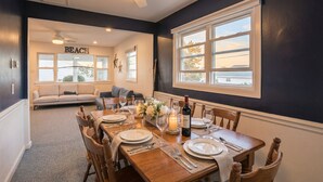 Comedor con mesa de madera dispuesta para seis comensales, una araña y vistas al exterior.