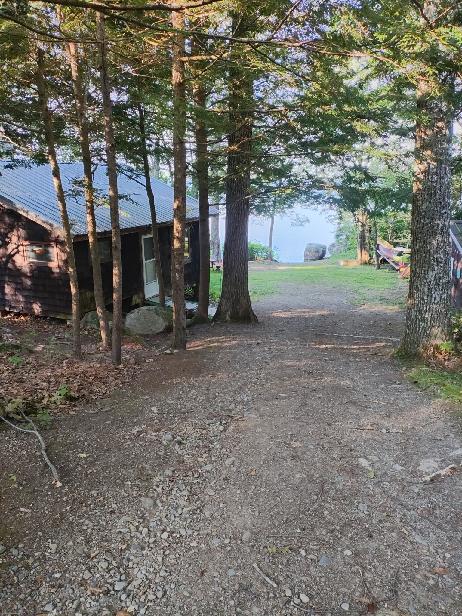 A rustic cabin with a gravel path leading to a dock by a lake.