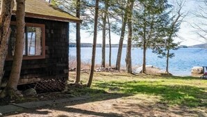 A rustic cabin with a wooden exterior, situated by a lake surrounded by trees. - Quaint Cottage on Swan Lake (Frankfort)