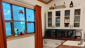 A kitchen with white cabinets, a wooden countertop, and a window with curtains. - Quaint Cottage on Swan Lake (Frankfort)