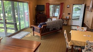 A cozy room with a bed, a TV, a dining table, and a large window. - Quaint Cottage on Swan Lake (Frankfort)