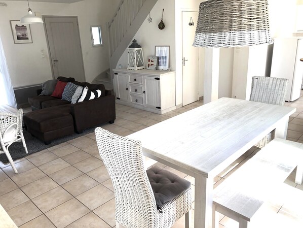 A spacious living area with a sofa, a dining table, and wicker chairs.