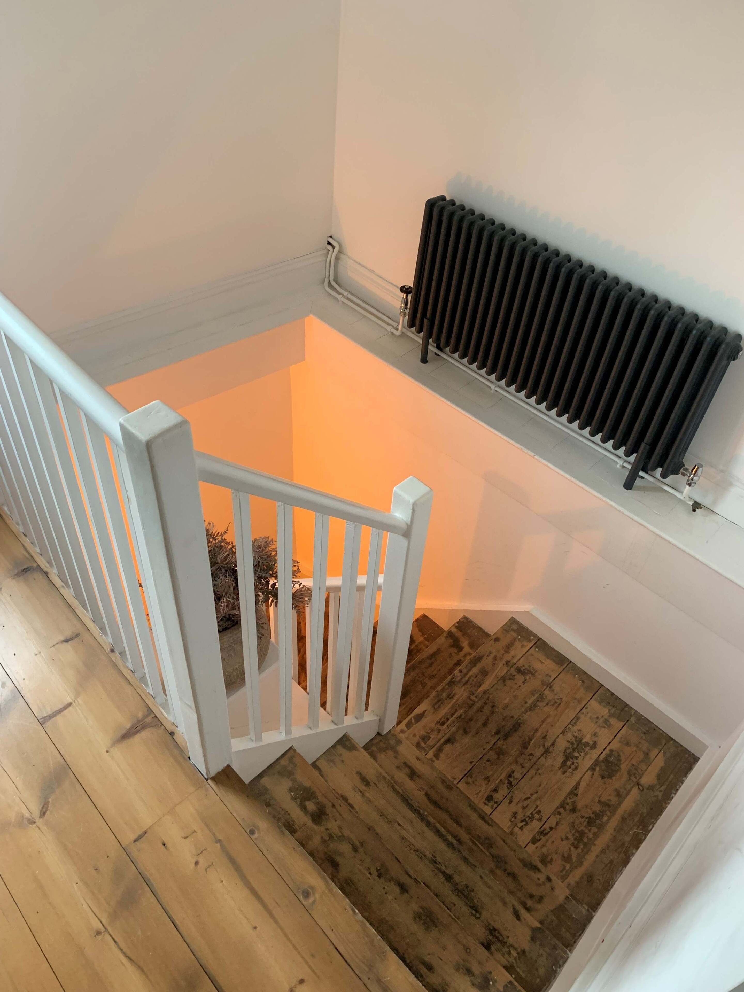 A wooden staircase with a white railing leading to a lower level. A radiator is mounted on the wall above the stairs.