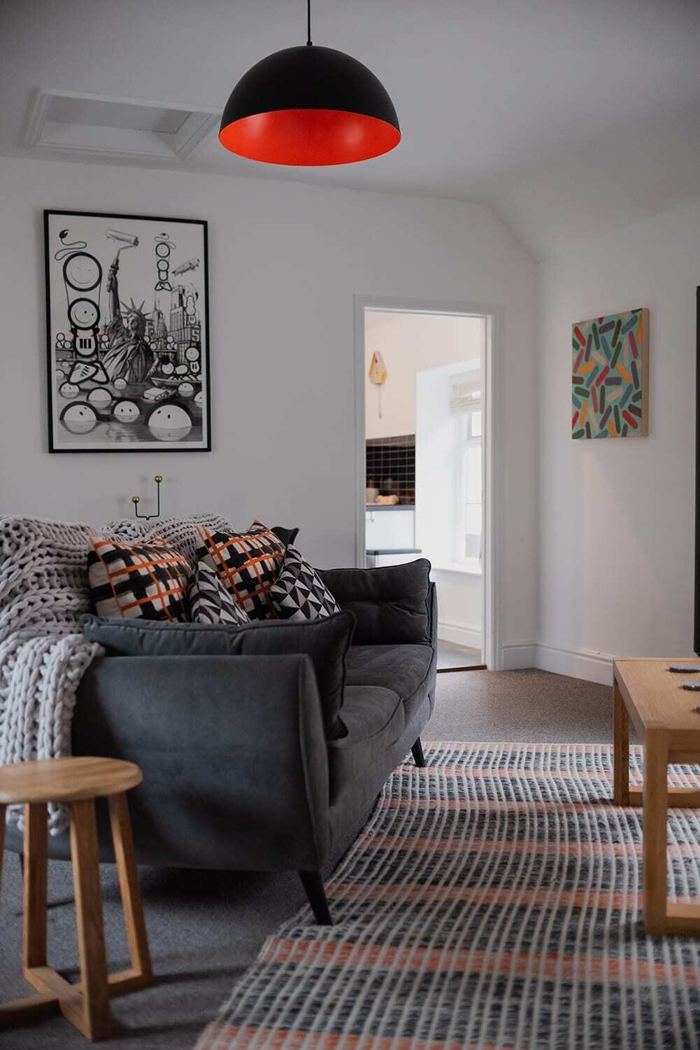 Een moderne woonkamer met een grijze bank, een zwart en rood hanglamp en een kamerbreed tapijt met dessin.