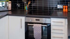 A modern kitchen with white cabinets, a black tiled backsplash, a stainless steel range hood, a built-in oven, and a microwave. - Grade II Listed Flat with Modern Touches Sleeps 2 (Norwich)