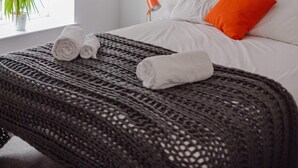 A neatly made bed with white and orange pillows, a black knitted throw, and a red pendant light above. - Grade II Listed Flat with Modern Touches Sleeps 2 (Norwich)