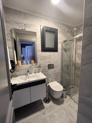 A modern bathroom with a marble sink, a glass shower enclosure, and a framed mirror above the sink.