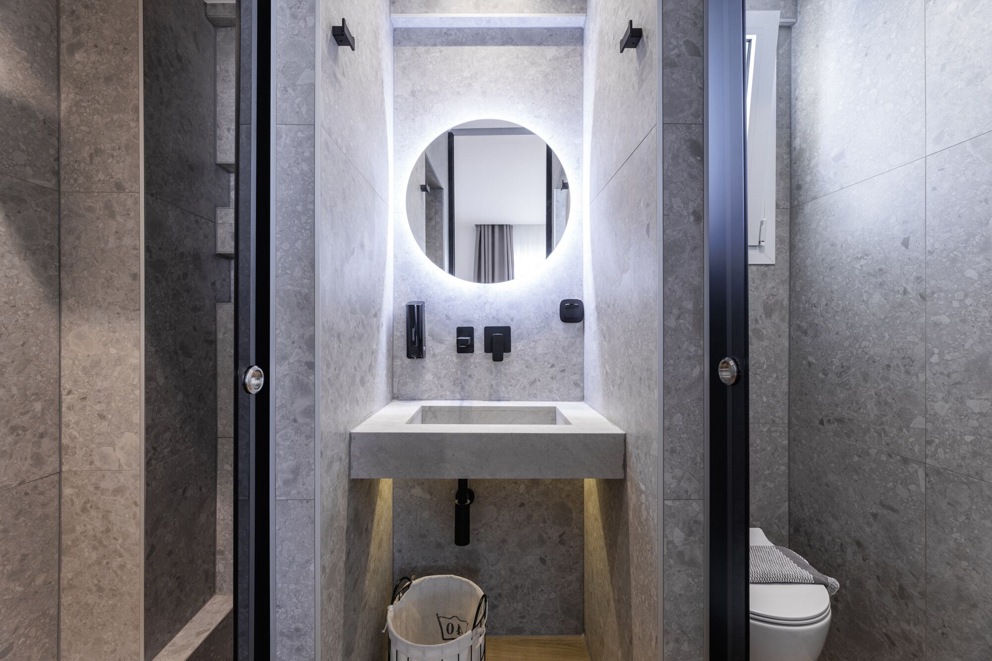 A modern bathroom with a rectangular sink, a round mirror, and a toilet.