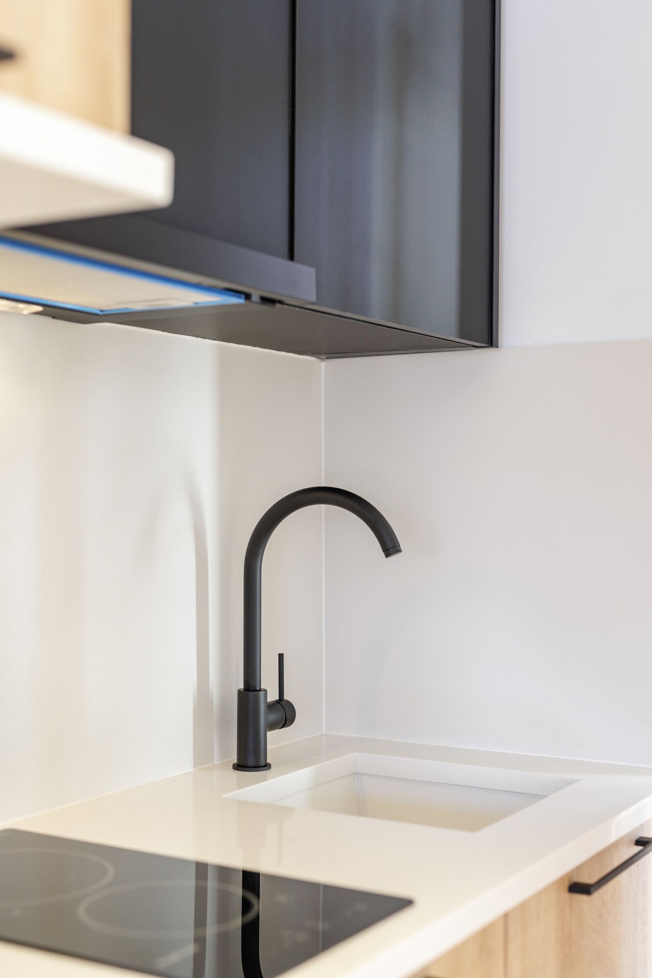 A modern kitchen with a sleek black faucet, white countertop, and stainless steel cabinets.