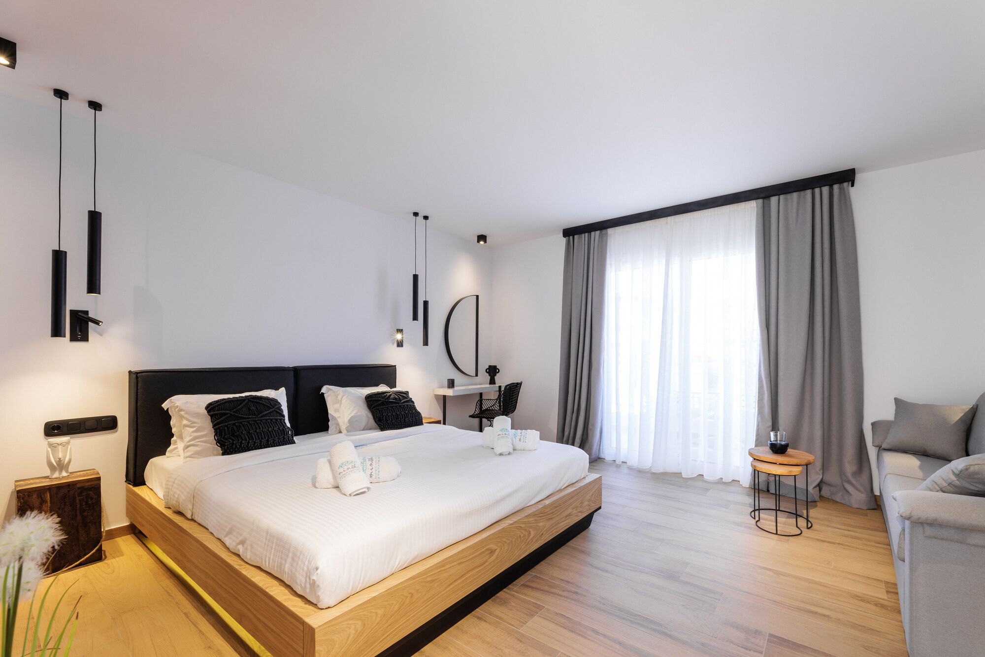 Una habitación de hotel moderna con una cama grande, una mesita pequeña, una silla y un escritorio con otra silla.